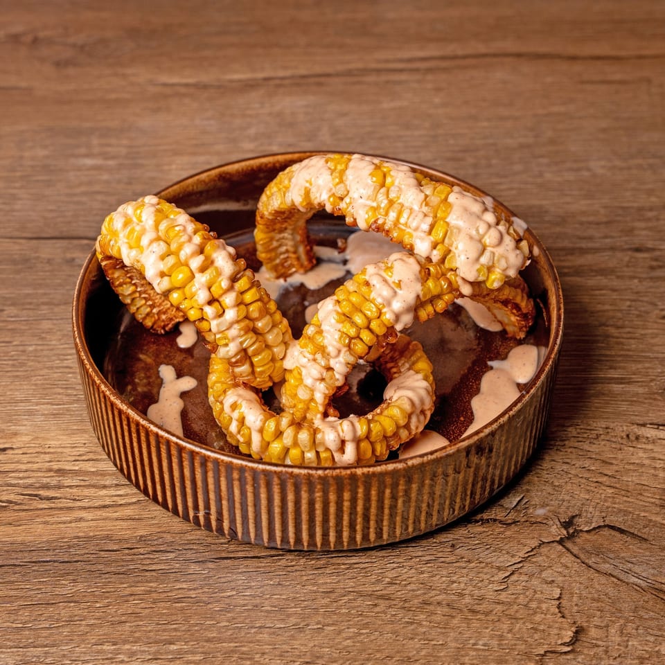 Grilled corn on the cob, cut into pieces and drizzled with a creamy sauce in a brown bowl.