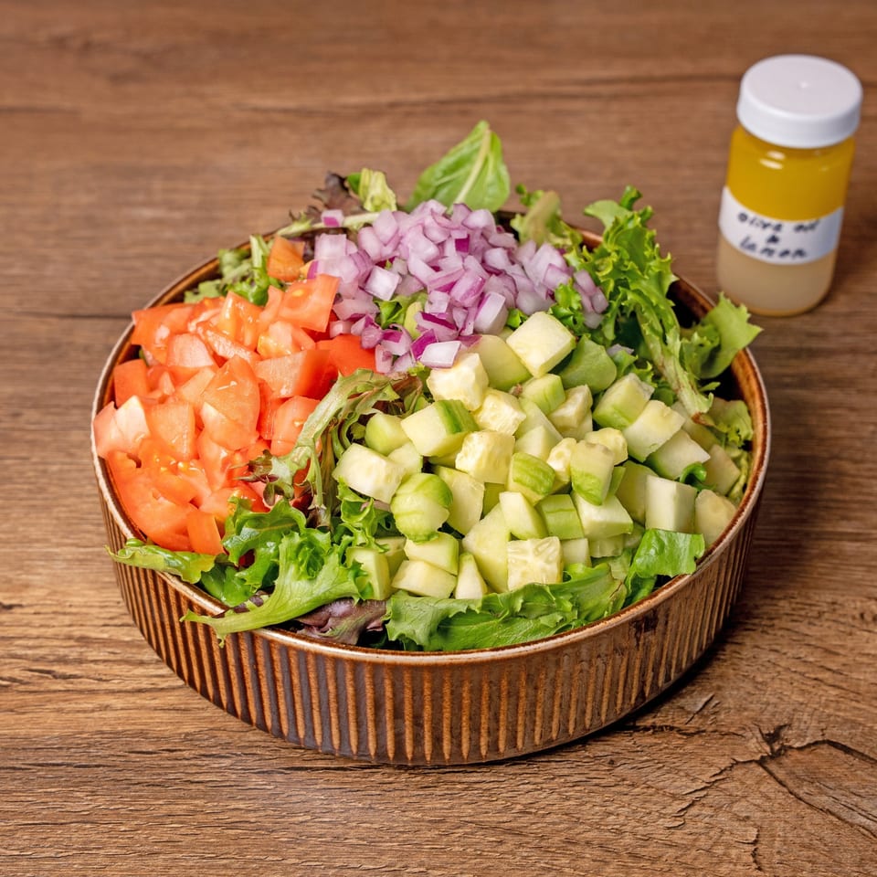 A fresh salad with diced tomatoes, cucumbers, red onions, and mixed greens, with a side of dressing.