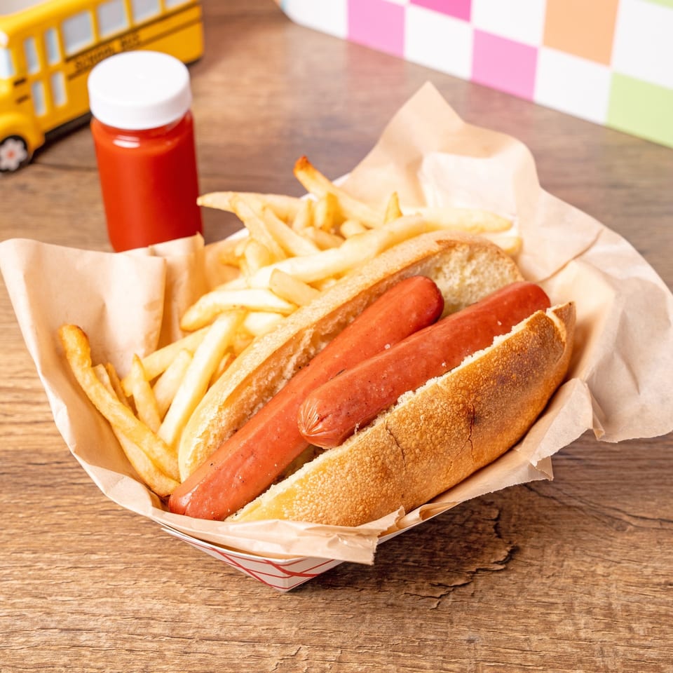 Two hot dogs in buns with a side of french fries and ketchup, on a wooden table.