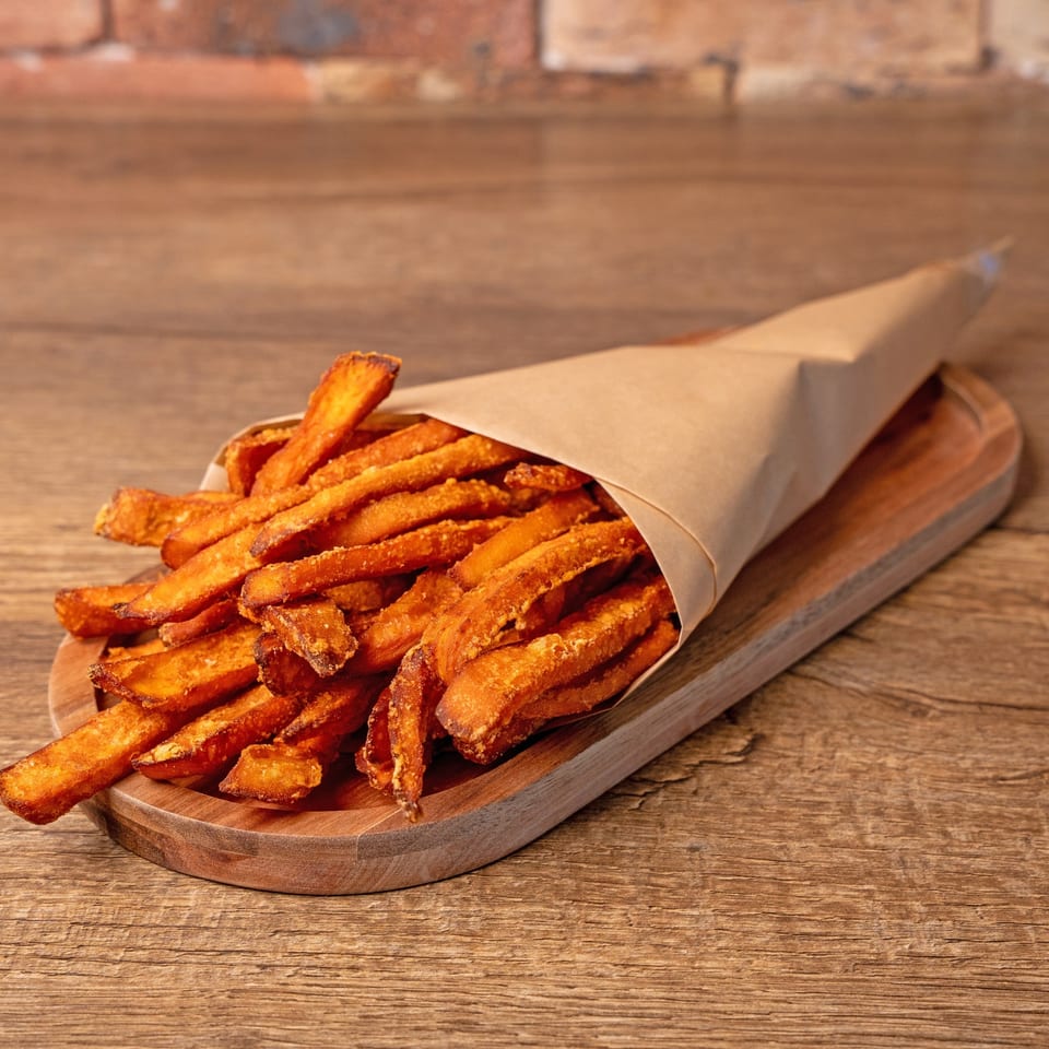 Crispy sweet potato fries in a brown paper cone, served on a wooden tray.