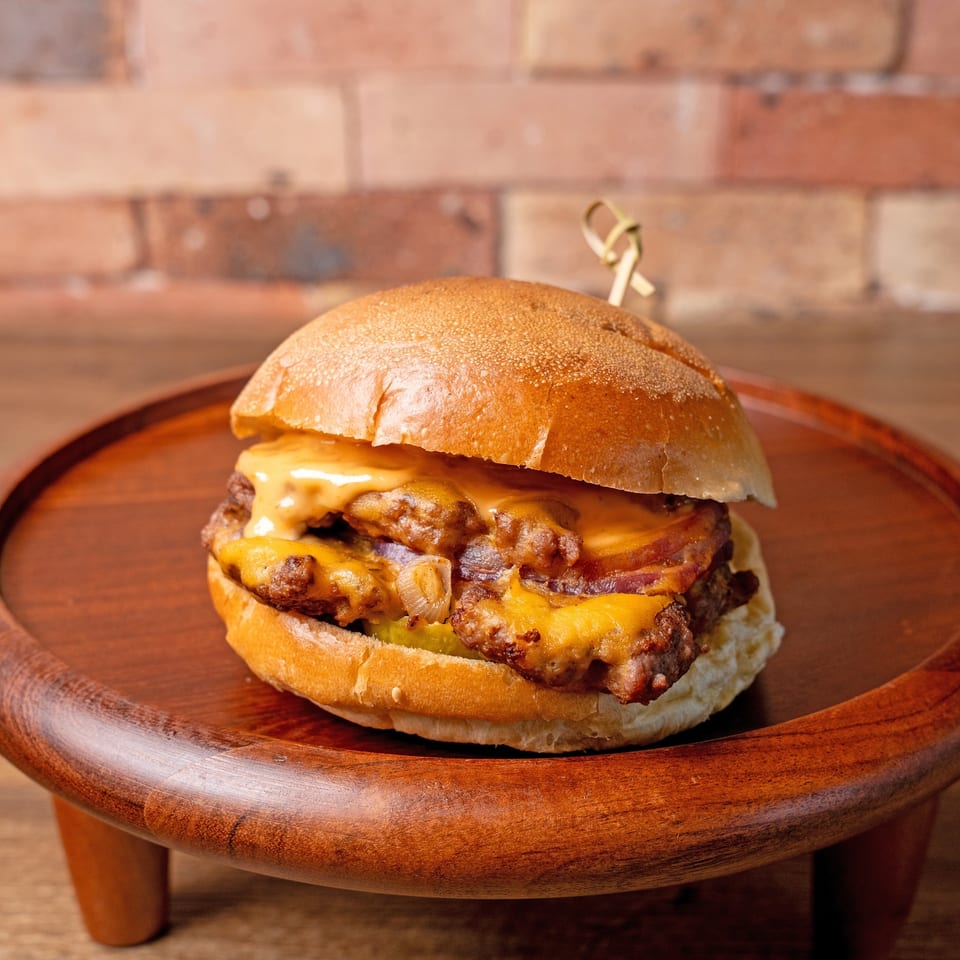 A double cheeseburger with melted cheese, bacon, and onions on a wooden serving tray.