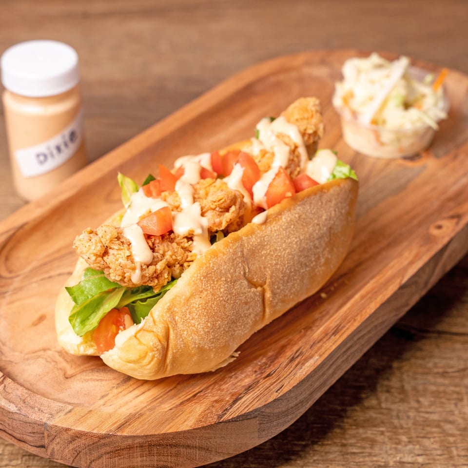 Crispy fried chicken po'boy with lettuce, tomatoes, and sauce, served with coleslaw and Dixie sauce.