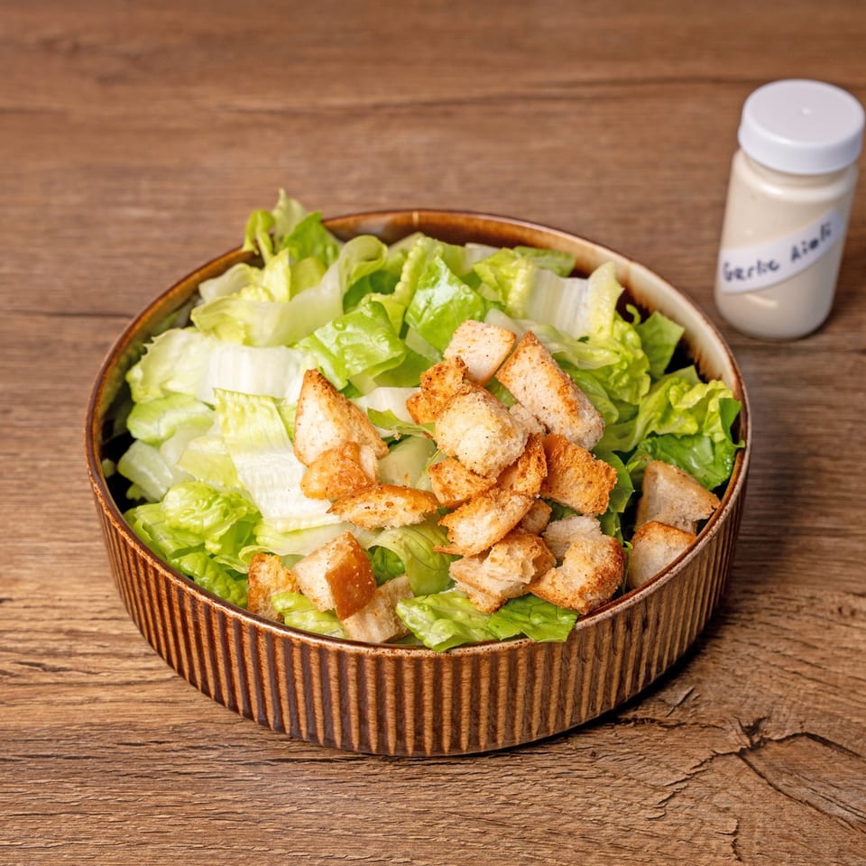 Fresh green lettuce and golden croutons in a brown bowl, with a small bottle of dressing.