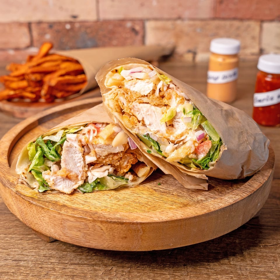Two chicken wraps with lettuce, onions, and sauce, served with sweet potato fries and dipping sauces.